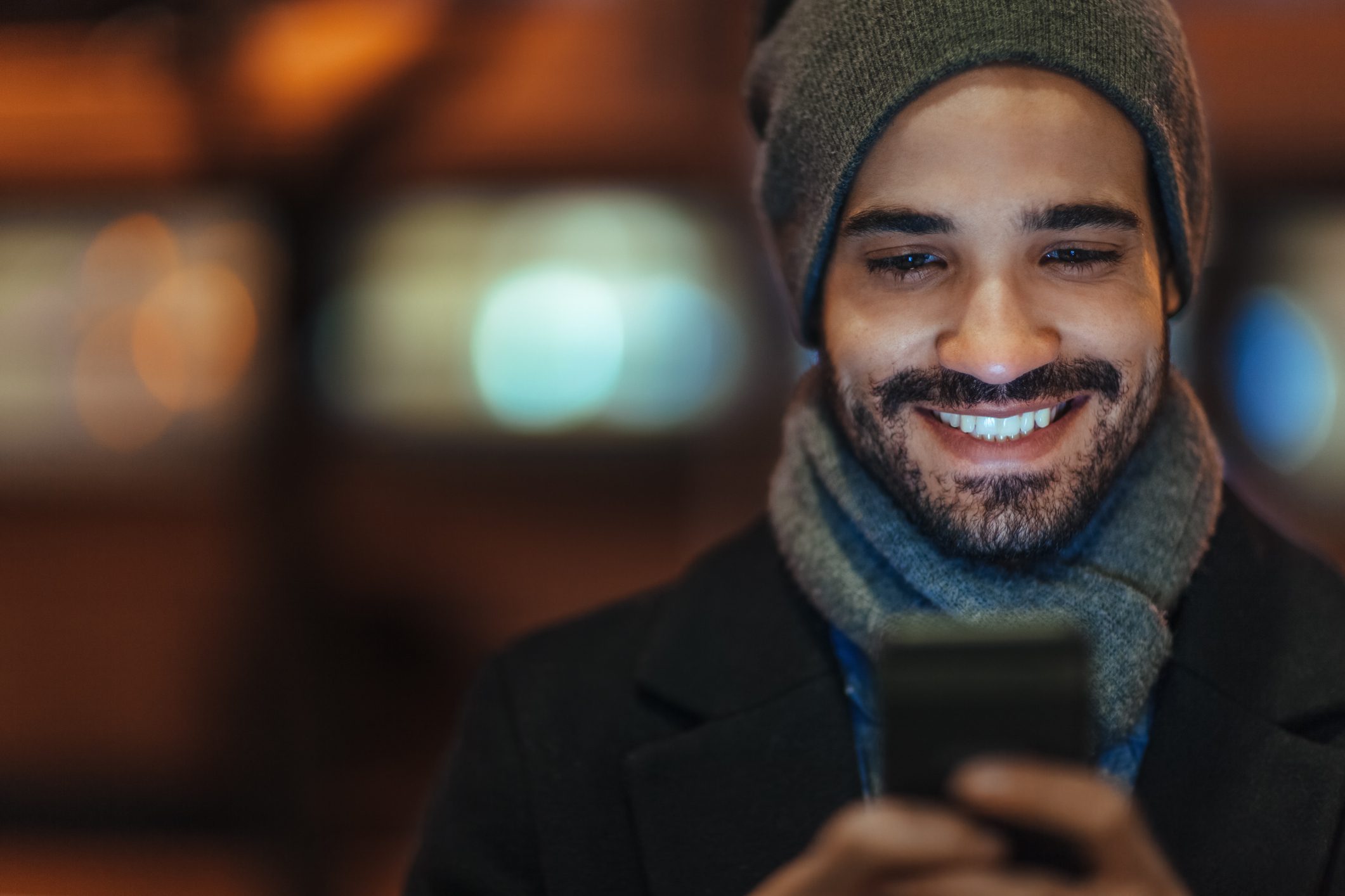 Young man smiling using smartphone on city street at night